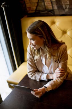 Dijital tabletli gülümseyen genç bayan kafede oturuyor.