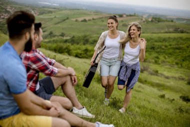 Çimlerin üzerinde oturan ve doğa gezisinde eğlenen bir grup genç insan.
