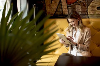 Dijital tabletli gülümseyen genç bayan kafede oturuyor.