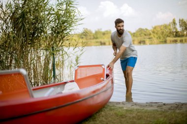 Yakışıklı genç adam sakin göle kano çekiyor.