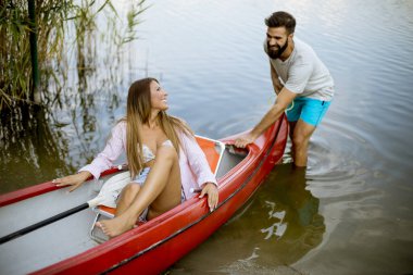 Yakışıklı genç adam genç bayanla kanoyu sakin göle çekiyor.