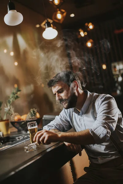 Man drinking beer and smoking cigarette at pub in the night