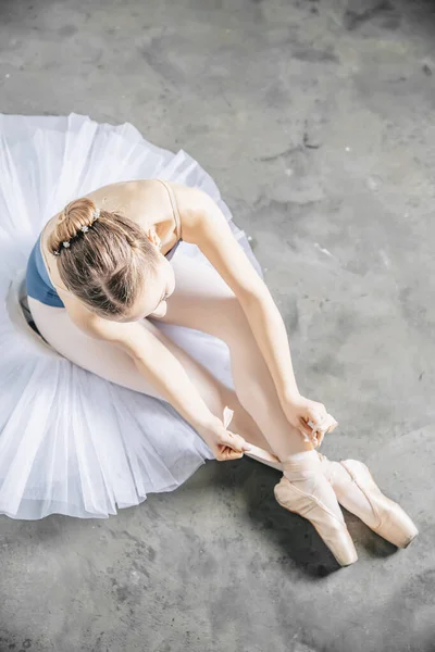 Top view at ballerina  tying slippers around her ankle and sitting on the floor