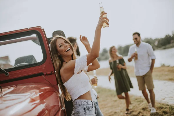 Happy young women drinks cider from the bottle by the convertible car with friends