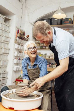 Çömlekçilik sınıfındaki bir öğretmenin yardımıyla çamurda dönen yaşlı bir kadın.
