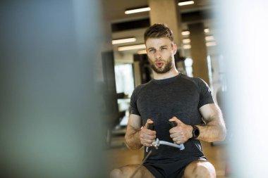 Yakışıklı genç adam spor salonunda oturan sıra makinesini kullanıyor.