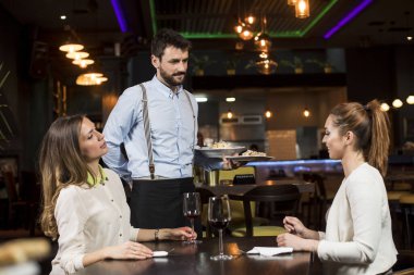 Restoranda yemek servisi yapan iki gülümseyen genç bayan arkadaş.