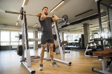 Yakışıklı genç sporcu spor salonunda halter kaldırıyor.