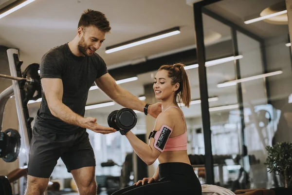 Çekici bir kadın ve spor salonunda ağırlık çalışması yapan kişisel bir antrenör.