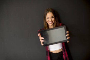 Duvarın yanında dijital tablet kullanan güzel, gülümseyen, uzun saçlı kadına bakın.