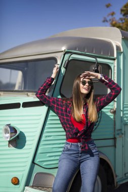 Gülümseyen güzel genç bayan klasik minivanın yanında duruyor.