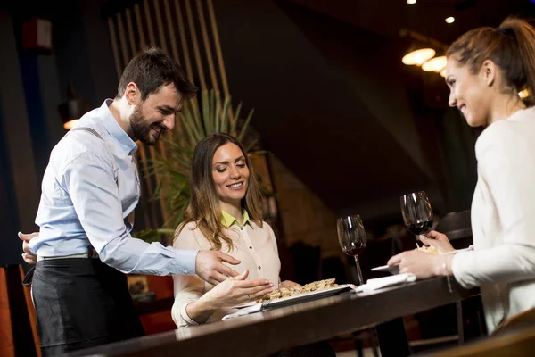 Dos Jóvenes Amigas Sonrientes Restaurante Con Camarero Sirviendo Cena —  Fotos de Stock