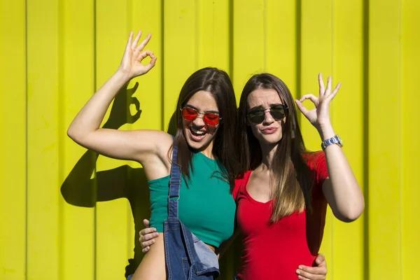 炎炎夏日 两个年轻貌美的姑娘站在黄色的墙边 — 图库照片