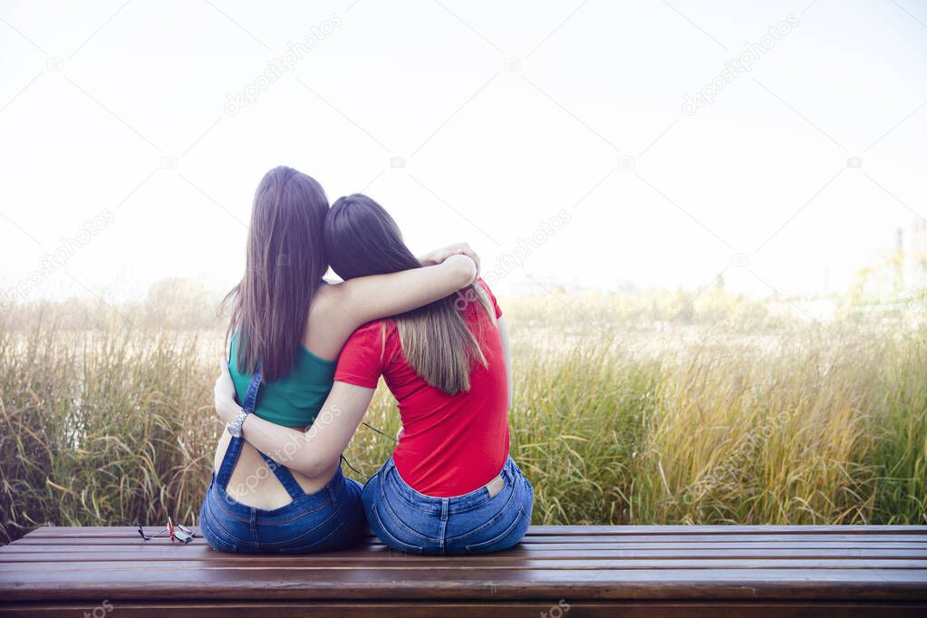 Two best female friends embracing together while sitting outdoors