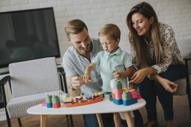 Anne ve babasıyla oturma odasında oyuncaklarla oynayan sevimli bir çocuk.
