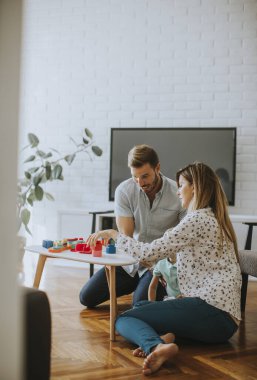 Anne ve babasıyla oturma odasında oyuncaklarla oynayan sevimli bir çocuk.