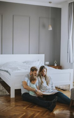 Genç ebeveynler küçük çocuğa kitap okuyor ve yerde eğleniyor.