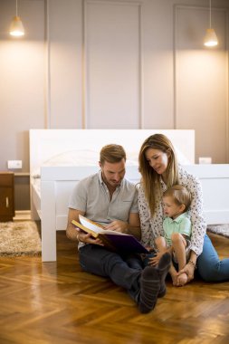Genç ebeveynler küçük çocuğa kitap okuyor ve yerde eğleniyor.