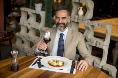 Yakışıklı olgun bir adam restoranda öğle yemeğinde kırmızı şarap içiyor.