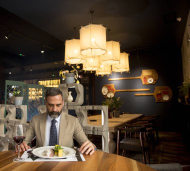 Yakışıklı olgun bir adam restoranda öğle yemeğinde kırmızı şarap içiyor.