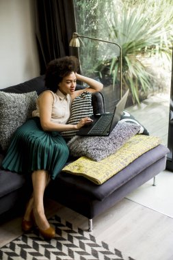 Kıvırcık saçlı güzel bayan, evdeki kanepede otururken defterde çalışıyor.