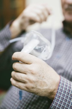 Üst düzey bir adam solunum maskesi ve nebulizatör kullanarak tıbbi ekipman kullanıyor.