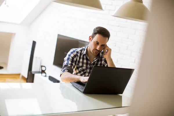 Jóképű Fiatalember Otthon Konyhaasztalon Laptopot Mobiltelefont Használ — Stock Fotó