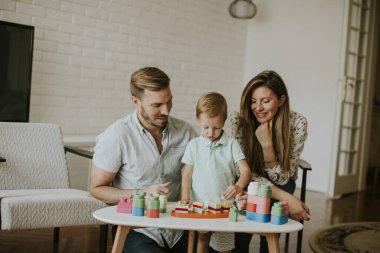 Anne ve babasıyla oturma odasında oyuncaklarla oynayan sevimli bir çocuk.