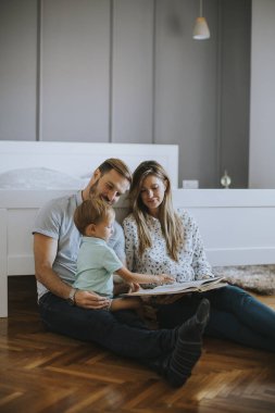 Genç ebeveynler küçük çocuğa kitap okuyor ve yerde eğleniyor.