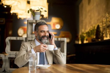 Yakışıklı iş adamı kafede kahve içiyor ve cep telefonu kullanıyor.