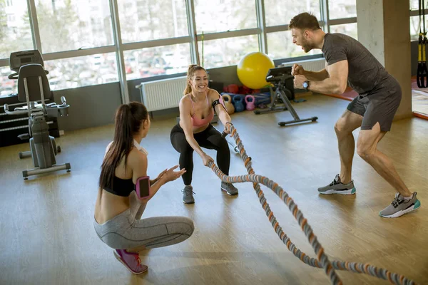 Pretty young woman with battle ropes exercise in the fitness gym witth support from her friends