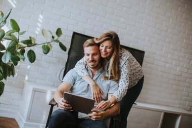 Oturma odasında dijital tablete bakan mutlu genç çift.