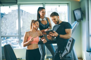 Dijital tablete bakan ve spor salonundaki genç kadınlara ilerlemeyi açıklayan kişisel antrenör.