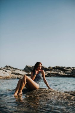 Deniz kenarındaki kayada oturan bikinili güzel bir kadın.