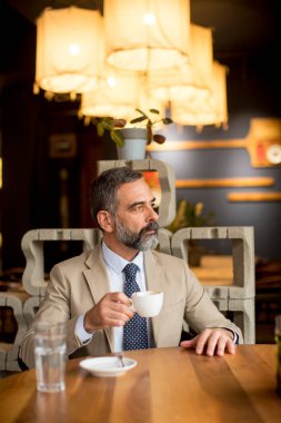 Düşünceli, yakışıklı, olgun iş adamı kafede kahve içiyor.