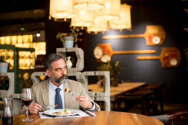 Yakışıklı olgun bir adam restoranda öğle yemeğinde kırmızı şarap içiyor.