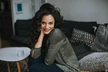 Masanın yanında kıvırcık saçlı, güzel genç bir kadın oturuyor.