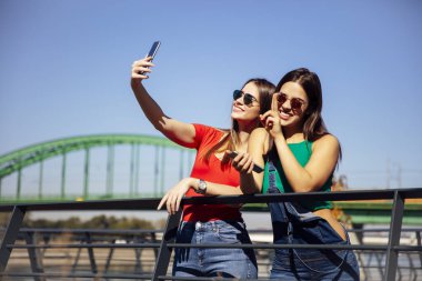 Gülümseyen genç bayan arkadaşlar bir yaz günü parkta selfie çekiyorlar.