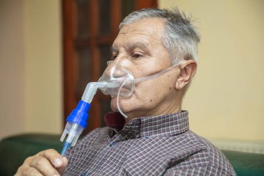 Üst düzey bir adam solunum maskesi ve nebulizatör kullanarak tıbbi ekipman kullanıyor.