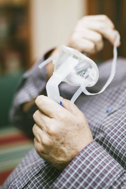 Üst düzey bir adam solunum maskesi ve nebulizatör kullanarak tıbbi ekipman kullanıyor.