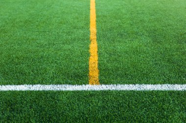 Yeşil suni çimen sahası, beyaz ve sarı çizgi sınırlı futbol sahası.