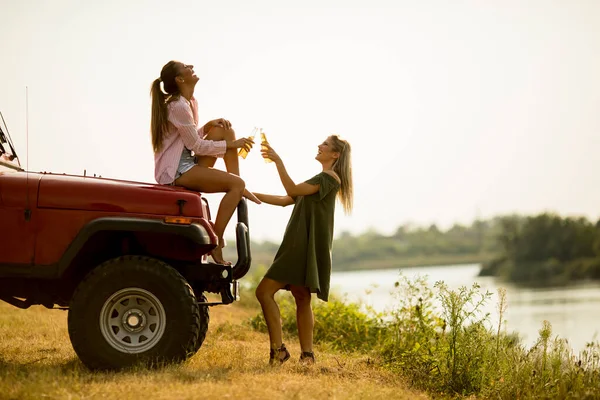 Две Счастливые Девушки Пьют Сидр Машины Берегу Озера — стоковое фото