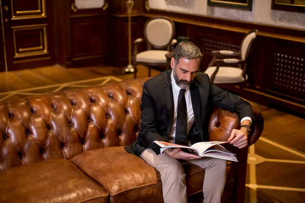 Przystojny Dojrzały Mężczyzna Eleganckim Garniturze Czytający Książkę Luksusowym Mieszkaniu — Zdjęcie stockowe