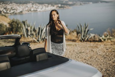 Cabriolet 'in deniz kenarındaki arabasına doğru yürüyen güzel genç bir kadın.