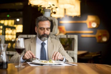 Yakışıklı olgun bir adam restoranda öğle yemeğinde kırmızı şarap içiyor.
