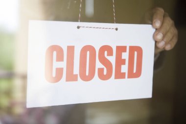 Dükkan sahibi cam dükkanının kapısında kapalı levhaya dönüyor.