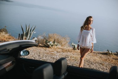 Cabriolet 'in deniz kenarındaki arabasına doğru yürüyen güzel genç bir kadın.