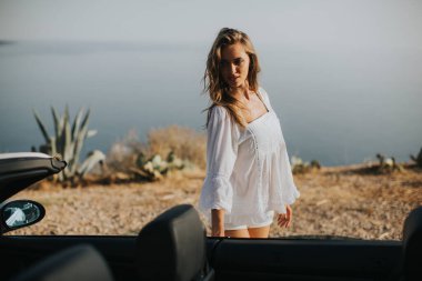 Cabriolet 'in deniz kenarındaki arabasına doğru yürüyen güzel genç bir kadın.