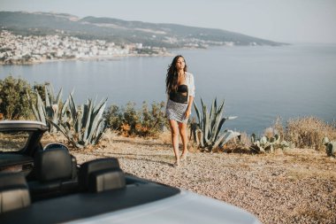 Cabriolet 'in deniz kenarındaki arabasına doğru yürüyen güzel genç bir kadın.