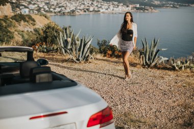 Cabriolet 'in deniz kenarındaki arabasına doğru yürüyen güzel genç bir kadın.